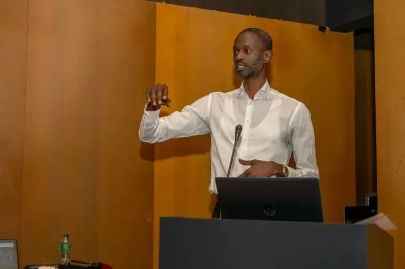 A speaker in a white shirt, hand raised, presents at the lectern