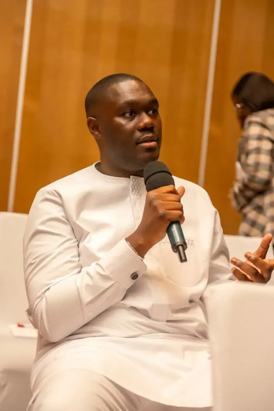 An attendee in light-coloured clothing speaks into the microphone in the room